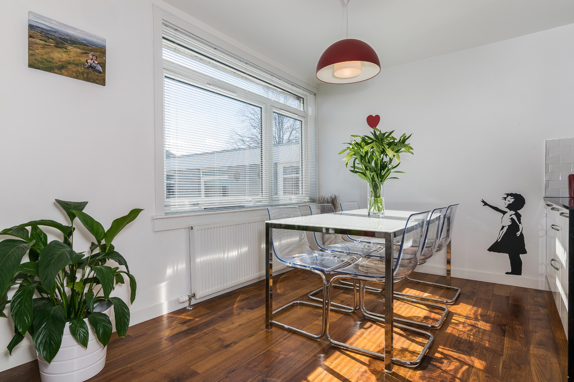 Glass dining table and clear chairs by a large window beneath a red pendant light at Mortonhall Road.