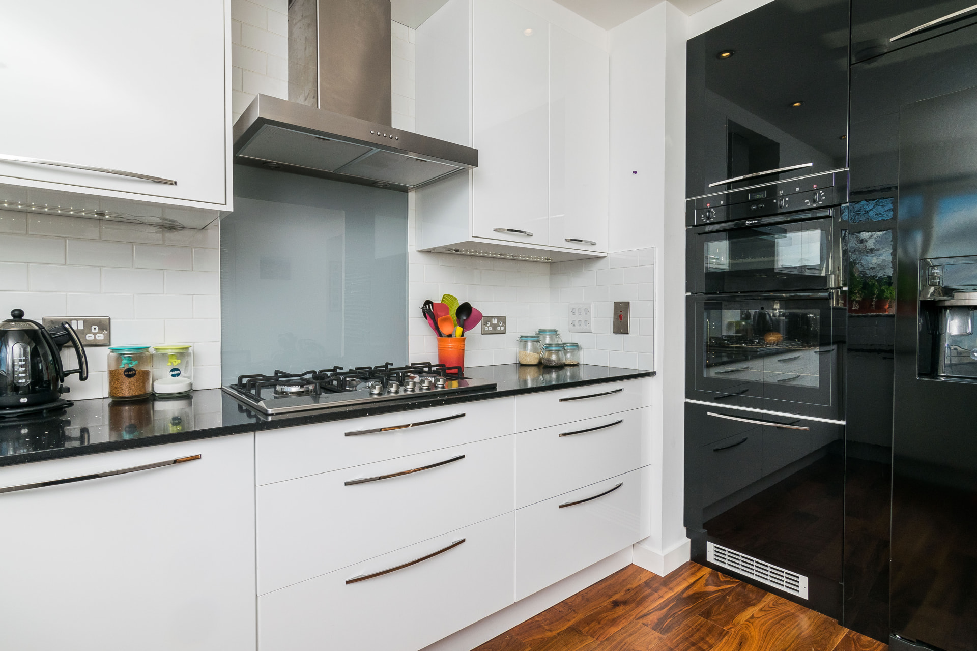 White kitchen cabinets and gas hob beside black tall cabinetry with integrated ovens at Mortonhall Road.